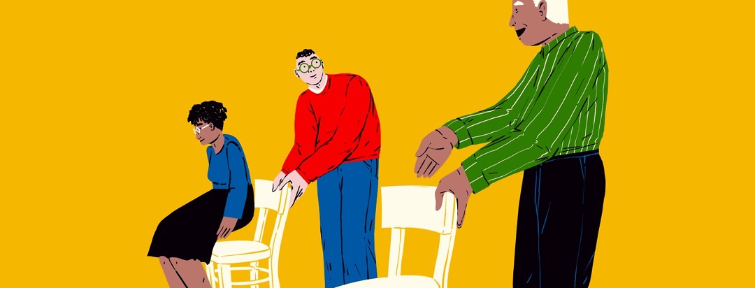 A male caregiver pulls out a chair for a woman, and looks over to his left where another man is pulling out a chair for the caregiver.