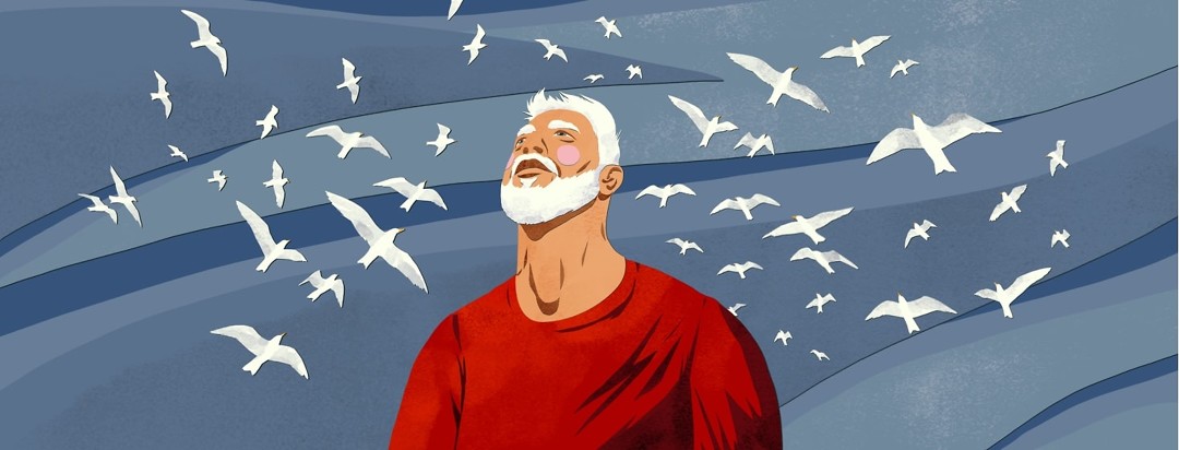 A man looks up toward the sky, which is full of flying seagulls.