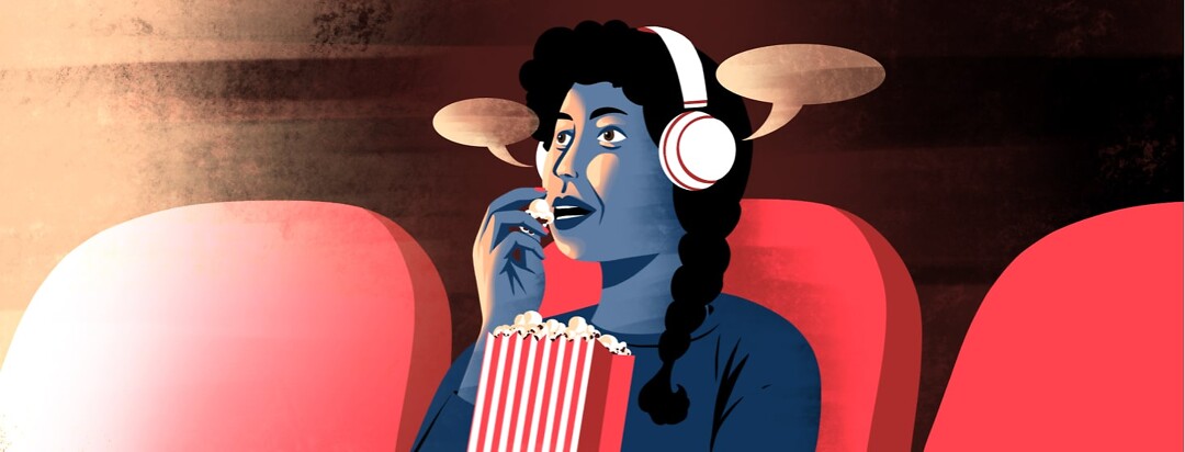 alt=A woman wearing headphones eats popcorn in a movie theater