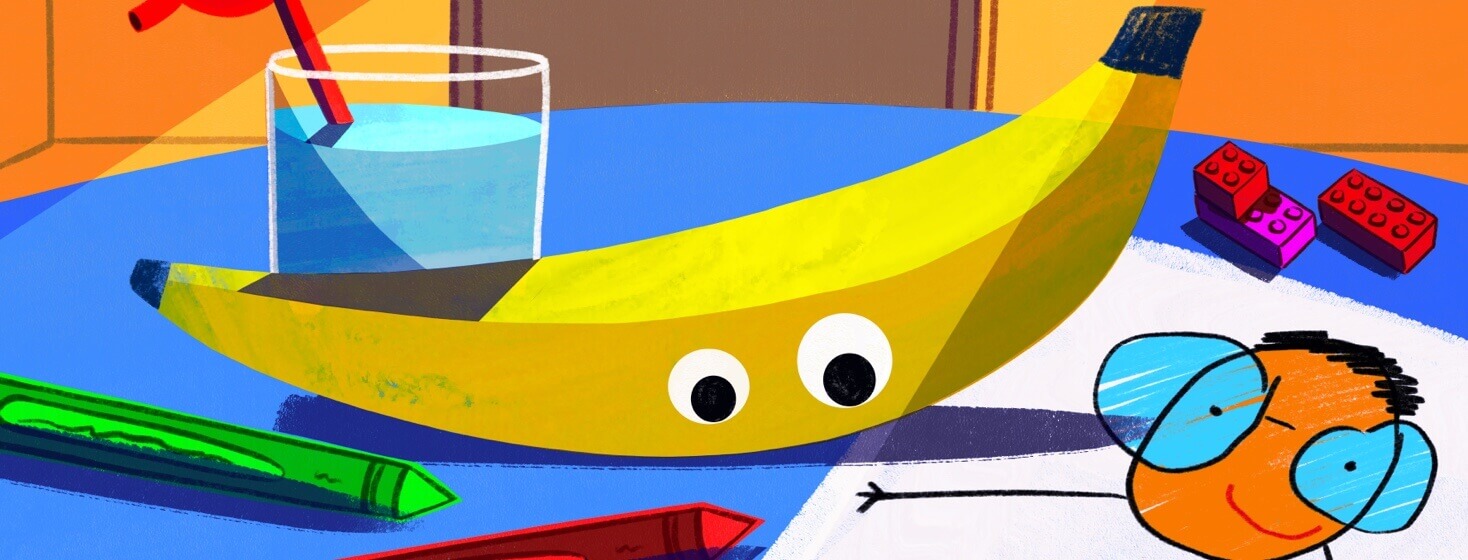 A banana with googly eyes sits on a table surrounded by crayons and children’s art