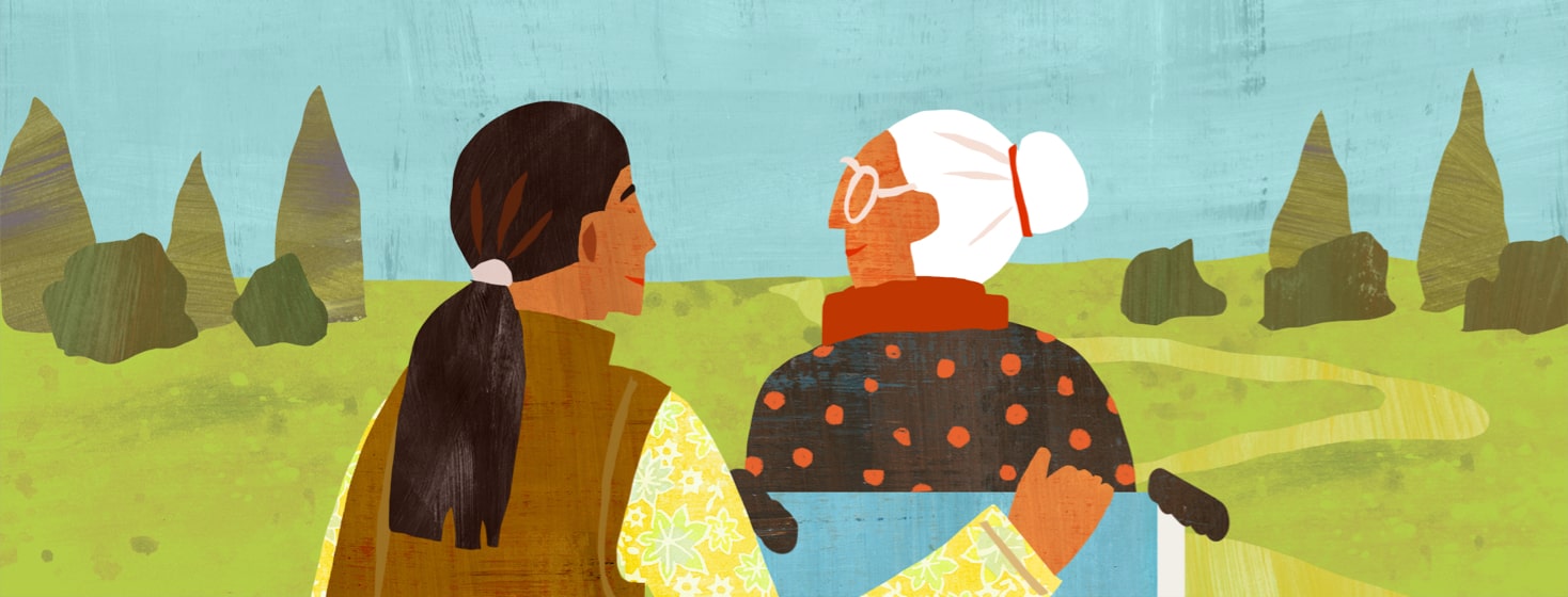 alt=a smiling younger woman crouches down to eye level for an elderly woman in a wheelchair, both in a grassy field with trees.