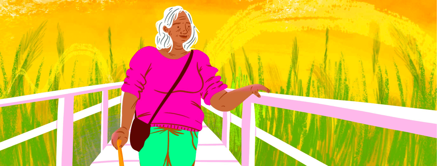 Elder woman on boardwalk walking with a cane smiles with sunset behind her